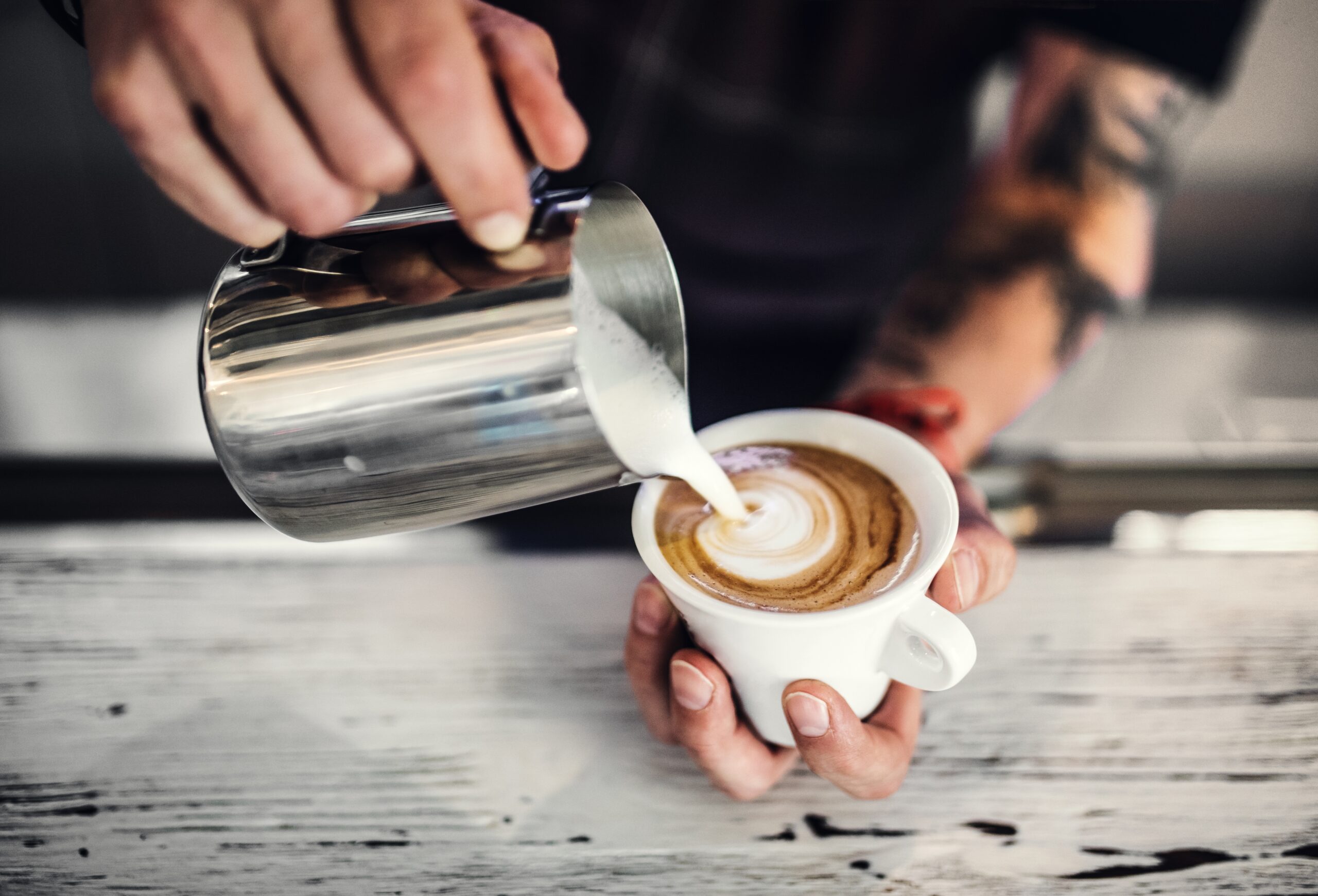 a person pouring milk into a cup of coffee in a coffee shop